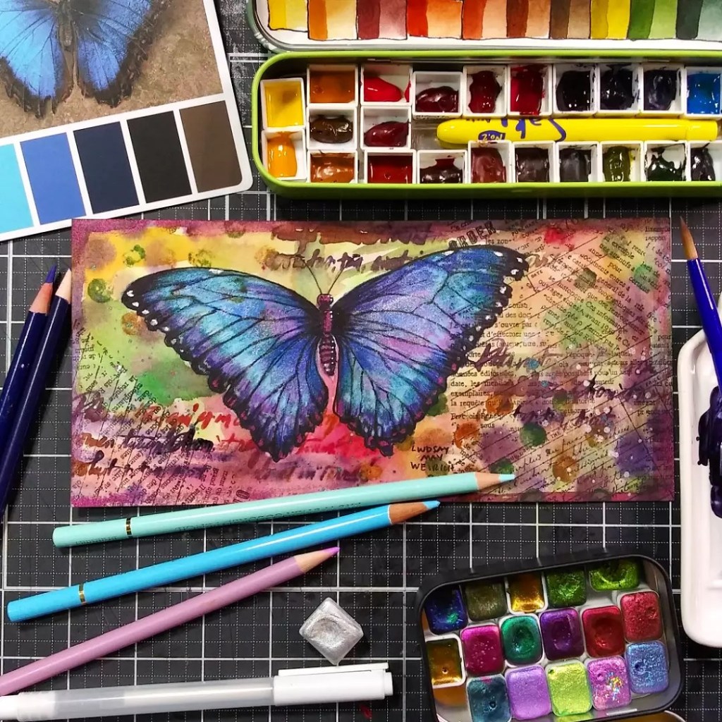 artsy watercolor painting of a butterfly surrounded by art supplies.