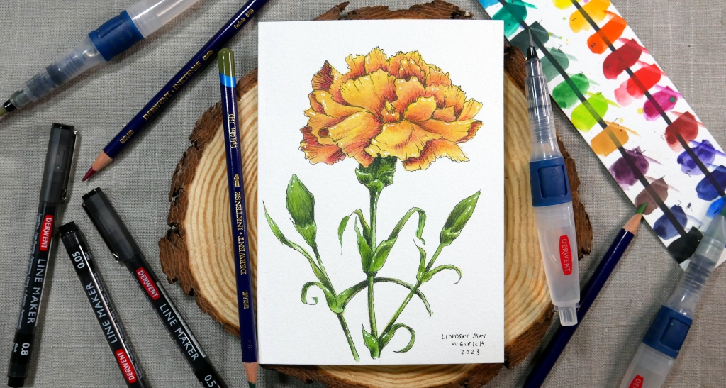 Ink and wash drawing of a carnation on a watercolor greeting card surrounded by art supplies.